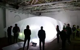 people in a theater space standing around a large glowing inflatable 