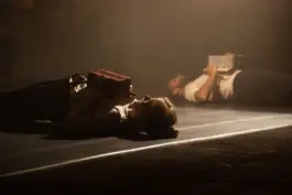 Two performer laying on the ground on a theater stage holding music instruments 